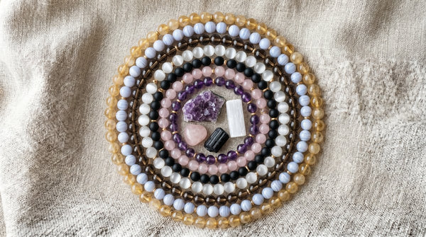 Stacked gemstone bracelets and crystals arranged in a circle on linen.