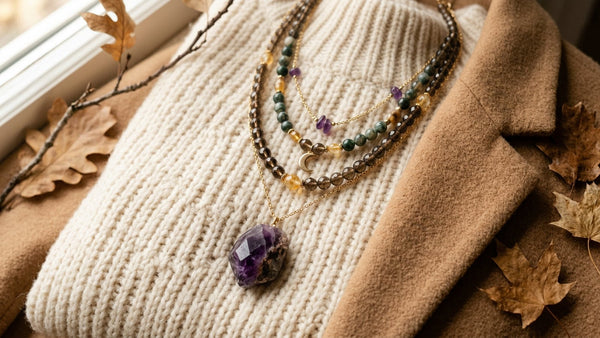 Layered crystal necklaces with colorful gemstone pendants styled on a warm autumn knit near dried leaves